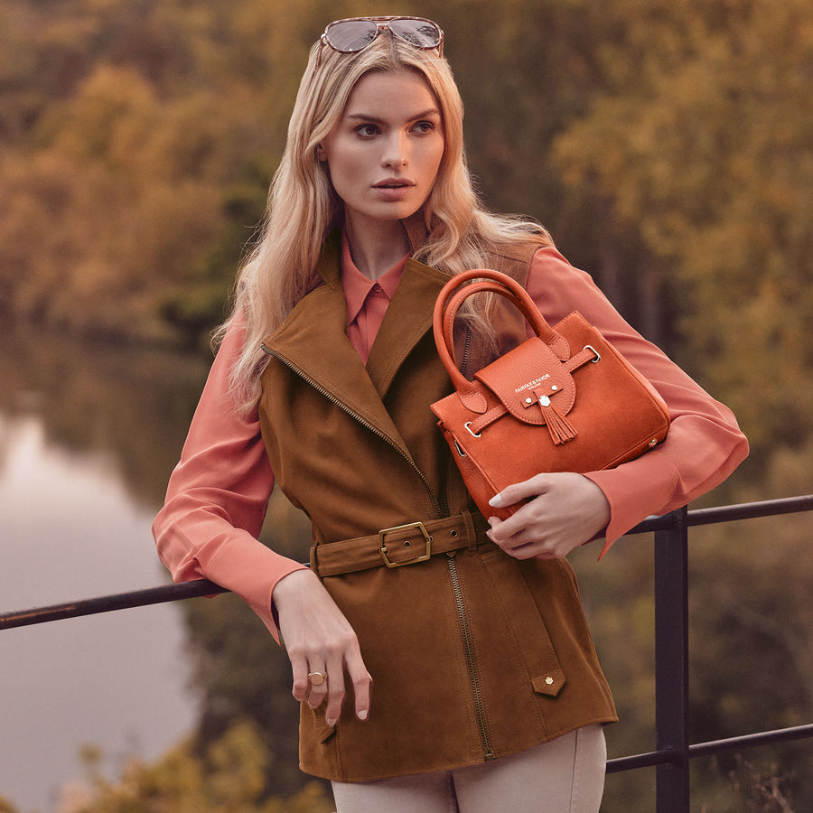 woman holding the Mini Windsor in Sunset and the Primrose gilet in tan, perfectly fitted looking very happy. 