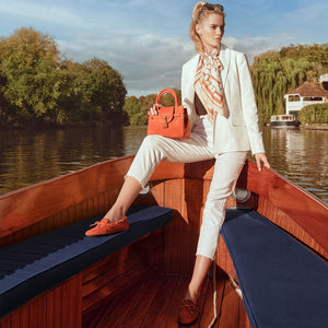 women holding the mini windsor in sunset, and wearing the sunset henley driving shoes, while on a boat in sunshine. 