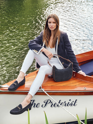 woman wearing the Tetbury crescent bag in navy suede, looking happy on boat.