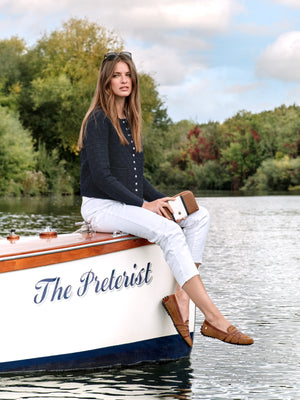 woman sittin on boat, showing off the rome driver shoes, a tan suede and leather shoe with a greek styled cross cross design. 