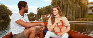 On a sunny day a man and woman are on a boat, happy, and holding Fairfax and Favor bag.